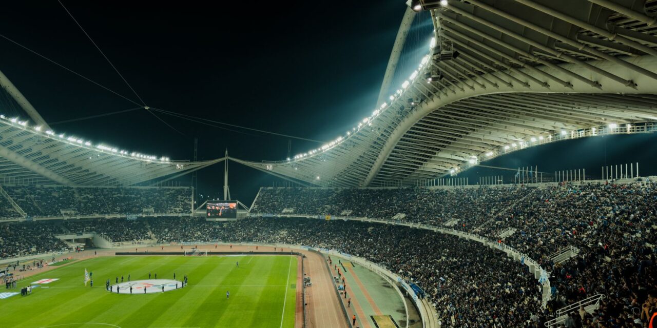 Gece oynanan bir futbol maçında ışıklarla aydınlanmış stadyum ve dolu tribünler